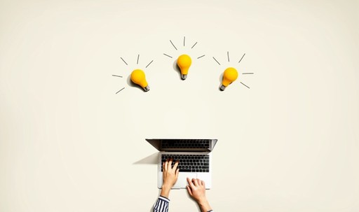 A person typing on a laptop with three yellow light bulbs above, symbolizing ideas or creativity. The light bulbs have lines around them, representing them being lit or active.