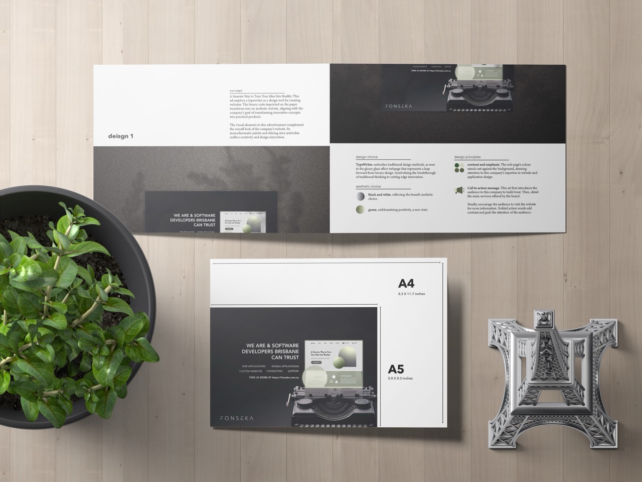A top-down view of a wooden desk with a potted green plant, an open brochure, graphical prints, a closed booklet labeled A4 and A5 Poster, and a metallic Eiffel Tower figurine. The brochures feature a typewriter image and tech-themed text.
