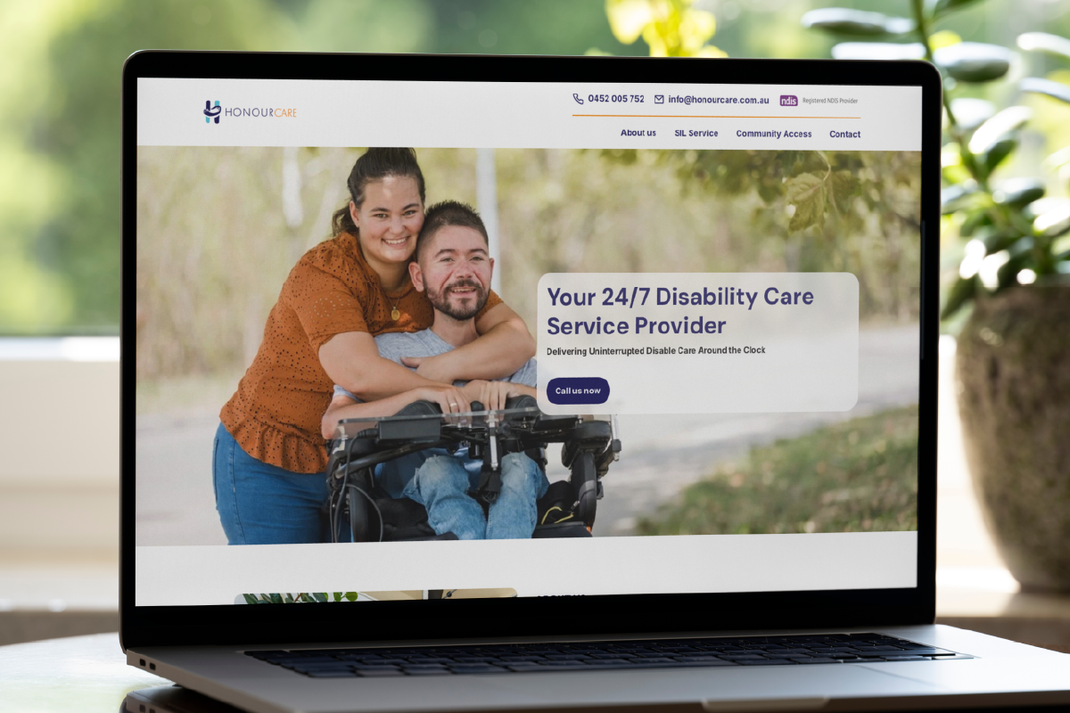 A laptop screen displays the HonourCare landing page for a 24/7 disability care provider, showing a smiling woman hugging a man in a wheelchair, with greenery in the background and contact information at the top.