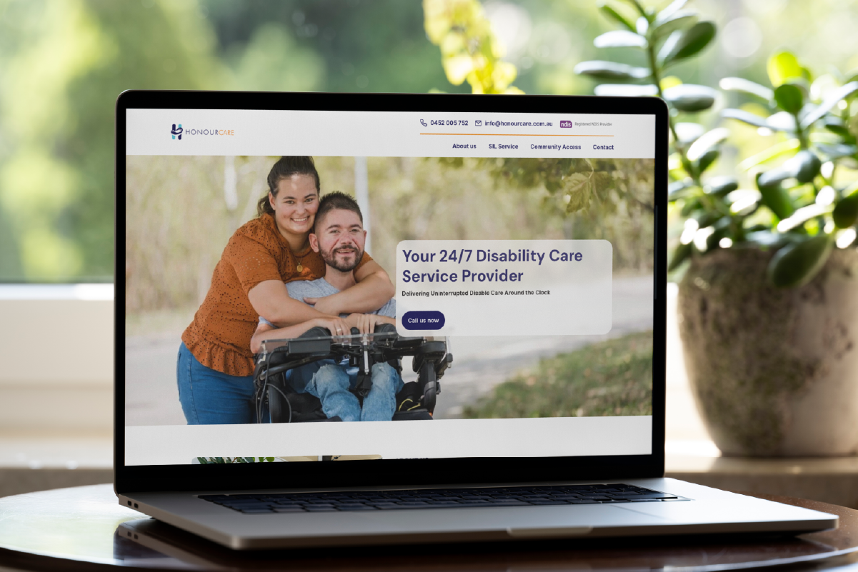 A laptop displays a website homepage for a 24/7 disability care service provider, featuring a woman smiling and hugging a man in a wheelchair, with greenery visible in the background.